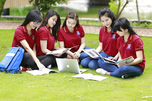 Nhóm sinh viên nữ mặc áo thun đồng phục màu đỏ đậm học bài trên bãi cỏ